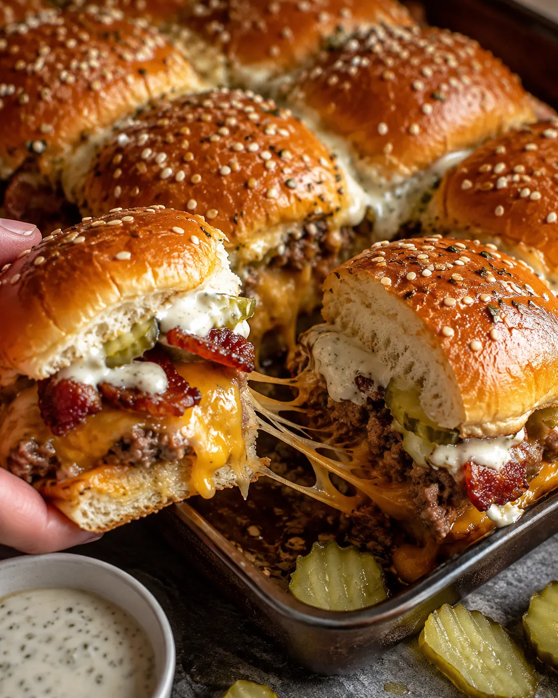 A person is holding a bacon cheeseburger pickle ranch slider.