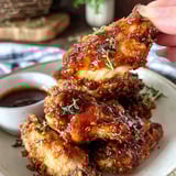 A person is holding a piece of hot honey chicken wings.