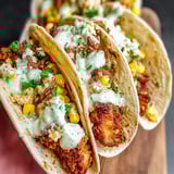 Two crispy chicken elote tacos on a wooden board.