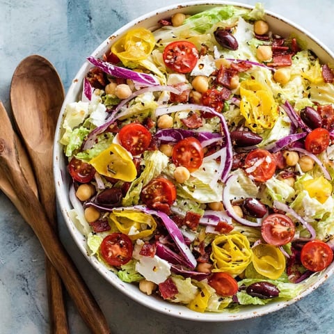 A bowl of salad with tomatoes, lettuce, chickpeas, and red onions.